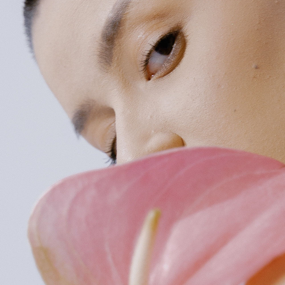 Refect Beauty Dermactive Acti-White Eye Contour gel applied to a model's skin near a pink anthurium flower