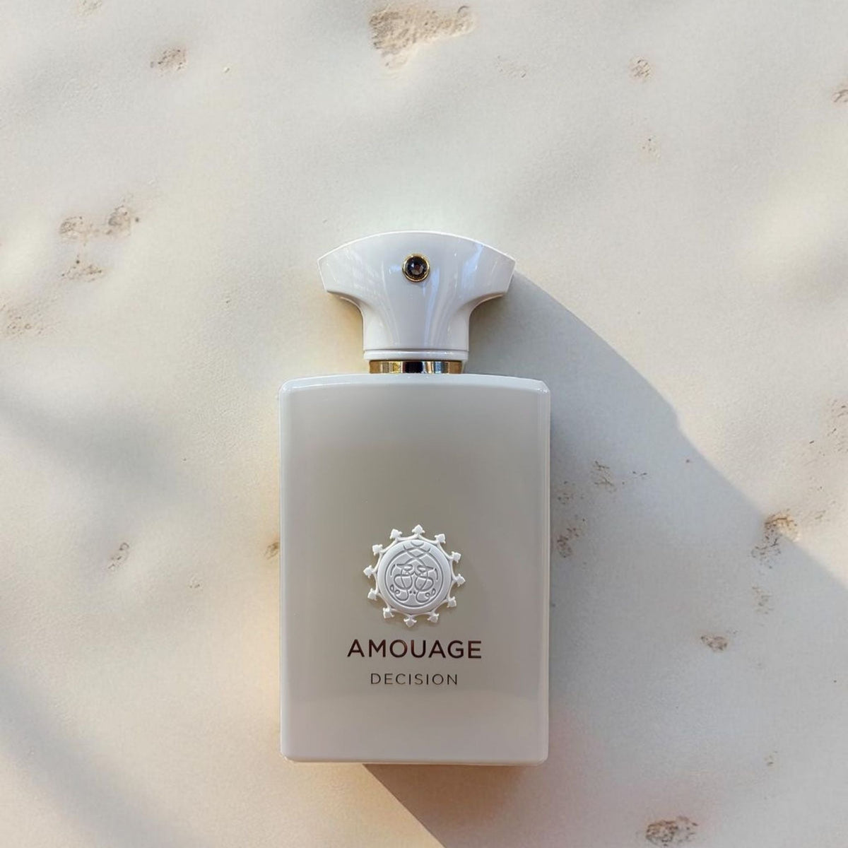 Refect Beauty Amouage Decision Eau de Parfum in a sleek white bottle with a unique emblem on a textured stone surface.