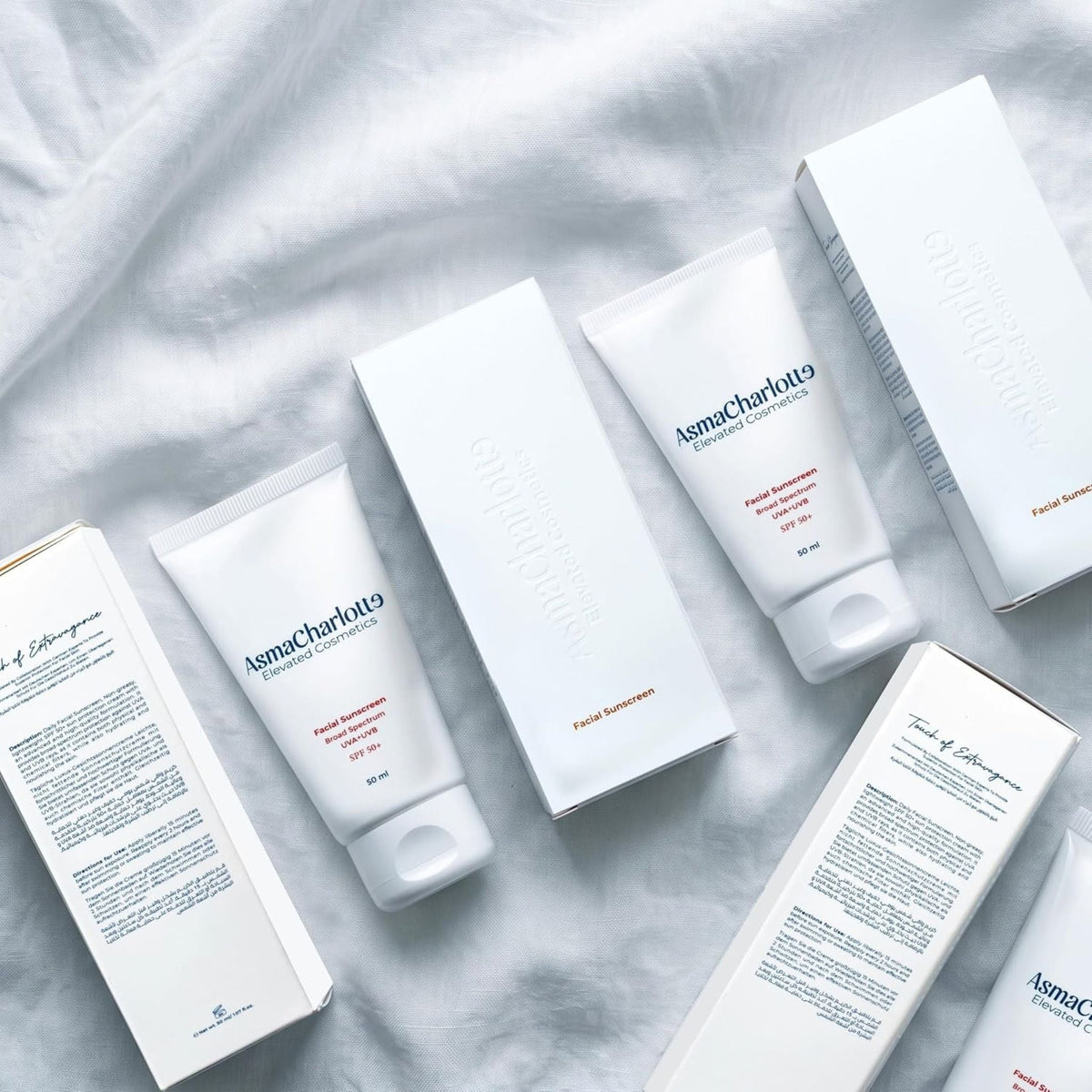 Refect Beauty AsmaCharlotte SPF 50+ facial sunscreen tubes and white product boxes on a soft fabric background.