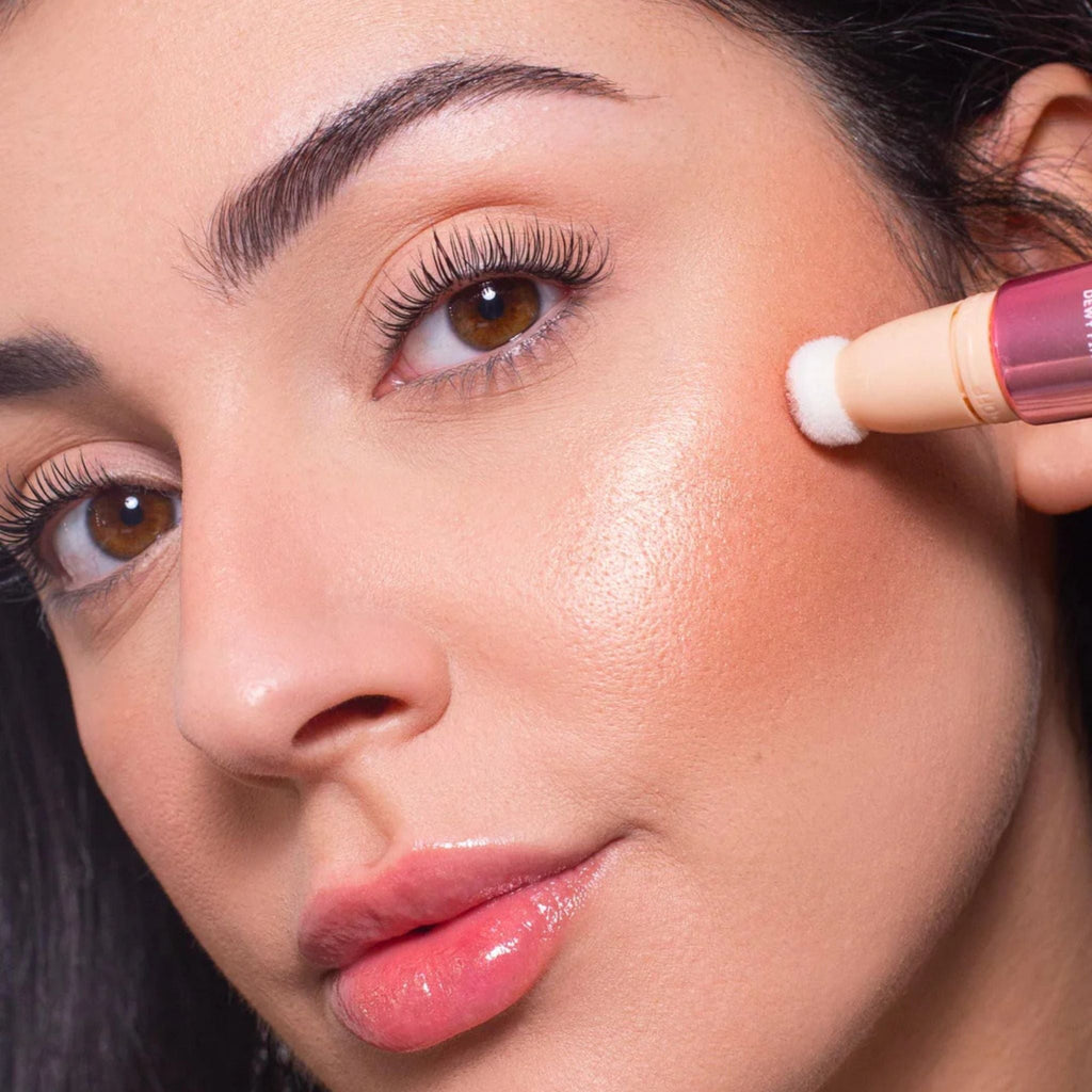 Refect Beauty Astra Light Therapy liquid highlighter being applied to a model's cheekbone with a sponge applicator.