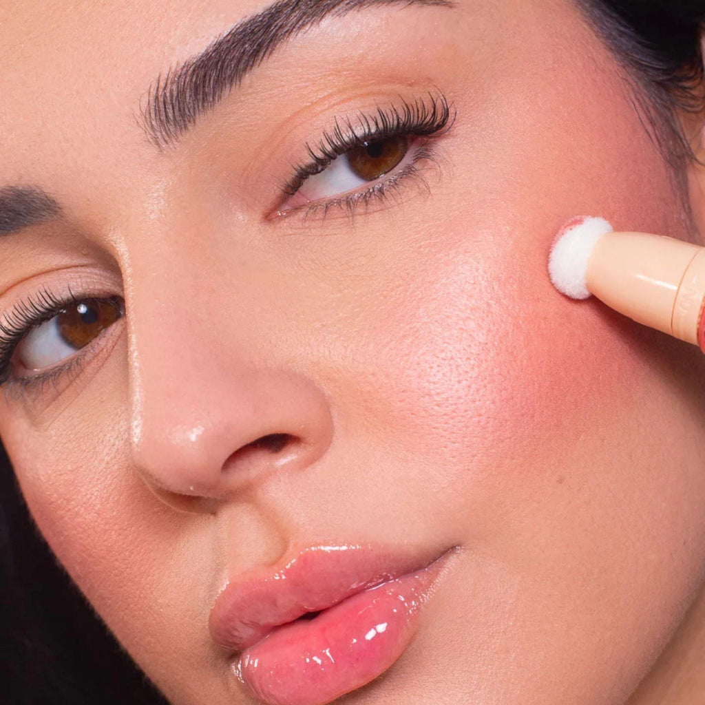 Refect Beauty Astra Light Therapy liquid highlighter being applied to a model's cheekbone with a sponge applicator