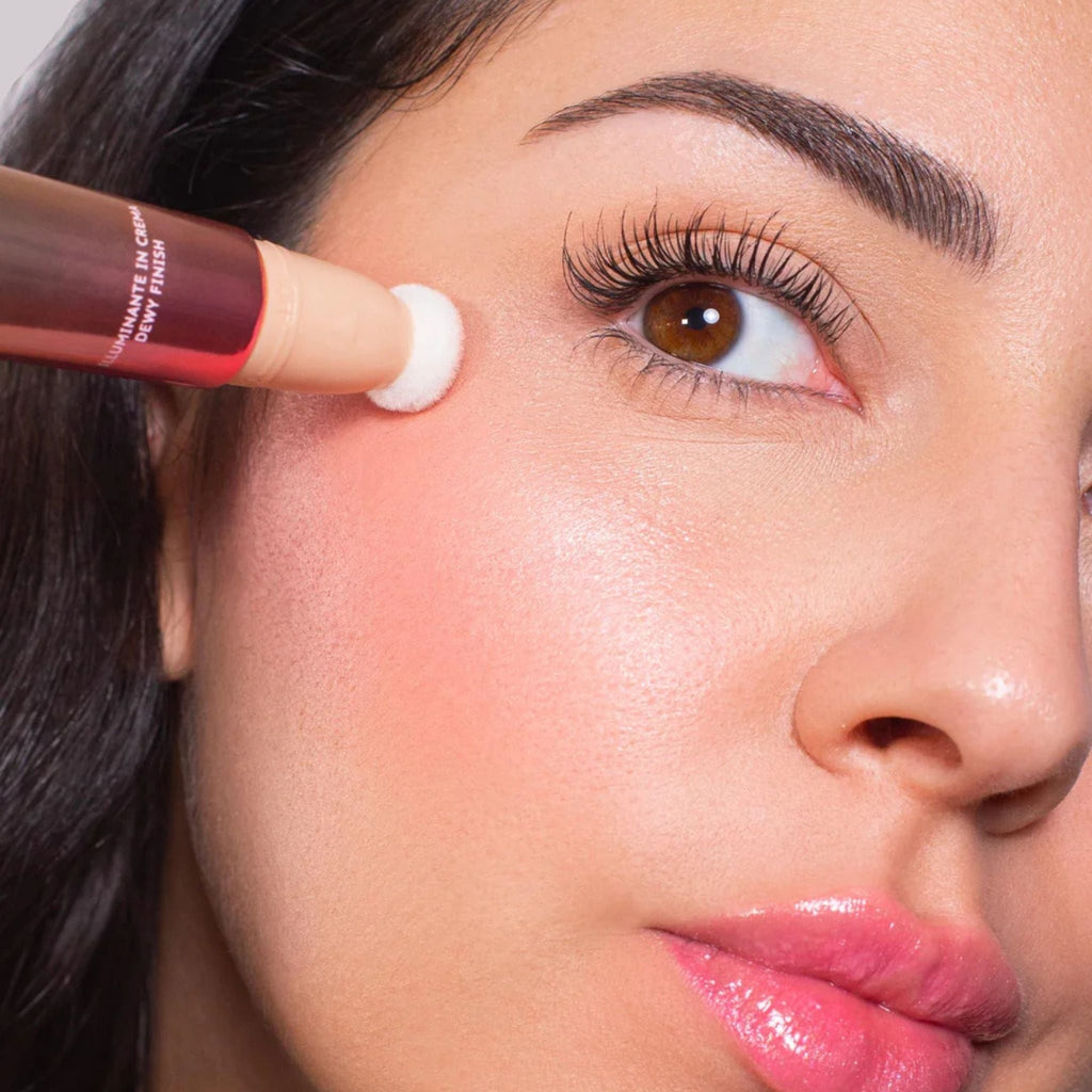 Refect Beauty Astra Light Therapy liquid highlighter being applied to a model's cheekbone with a sponge applicator.