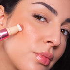 Refect Beauty Astra Light Therapy liquid highlighter being applied to a model's cheekbone with a sponge applicator.