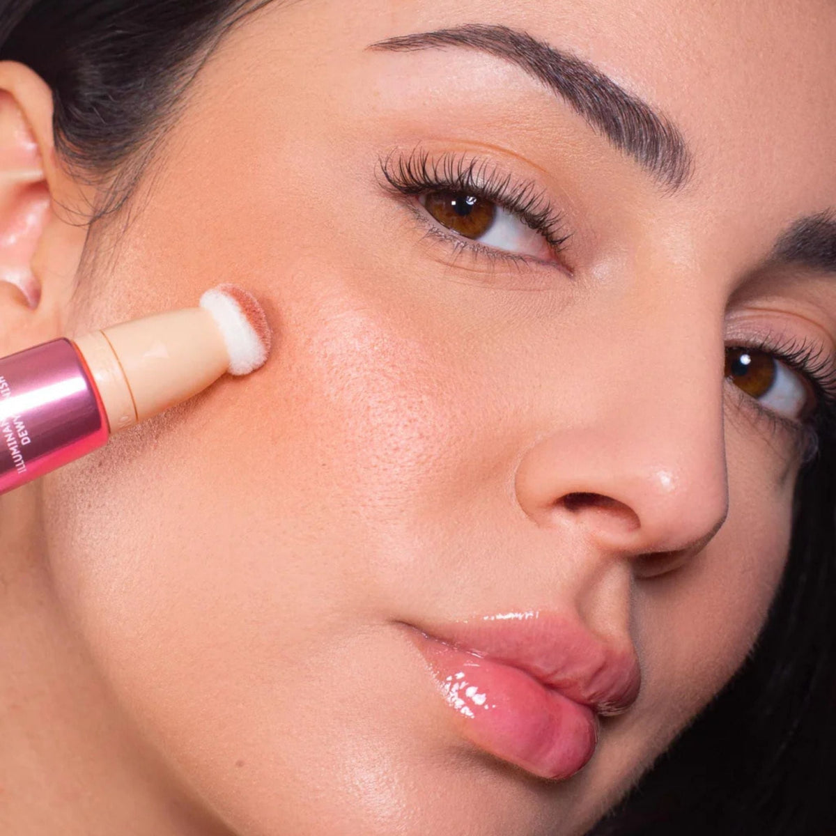 Refect Beauty Astra Light Therapy liquid highlighter being applied to a model's cheekbone with a sponge applicator.