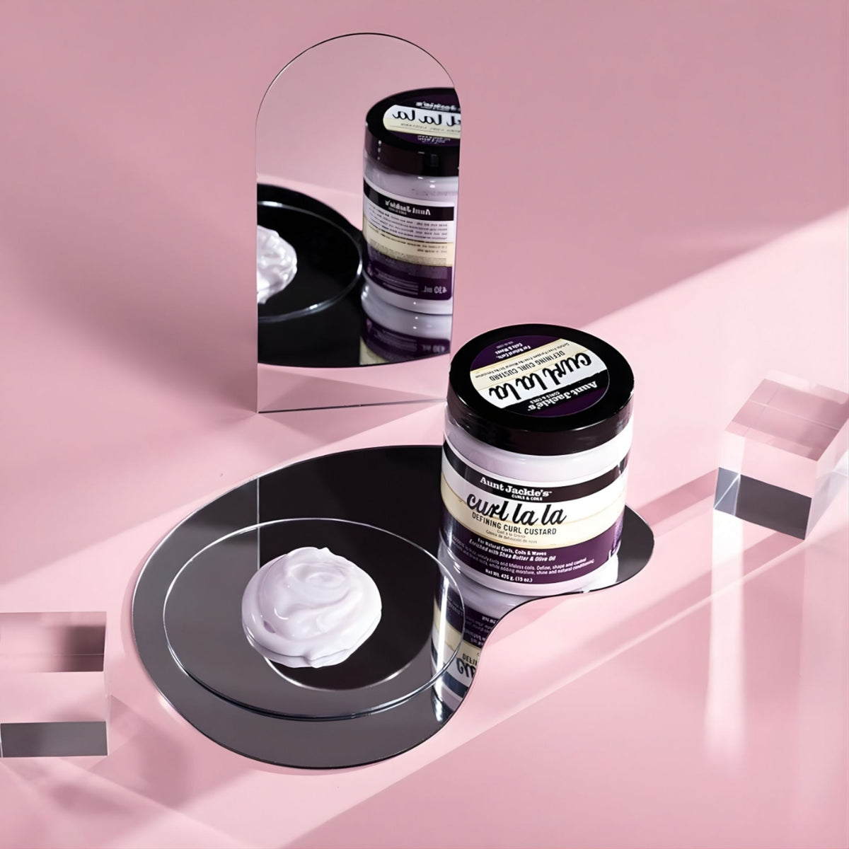Refect Beauty Aunt Jackie's Curl la la defining custard jar with cream texture on a mirror against a pink background.