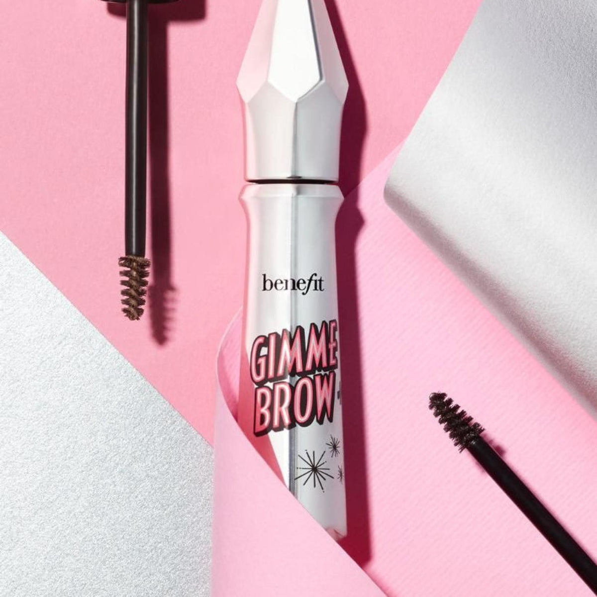 Refect Beauty Benefit Gimme Brow volumizing eyebrow gel in a silver tube with applicator brushes on a pink background