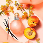 Refect Beauty Britney Spears Fantasy Naked perfume bottle surrounded by fresh peaches, vanilla beans, and flowers.