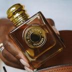 Refect Beauty Burberry Goddess Parfum in a square glass bottle with gold cap held against a brown leather bag