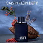 Refect Beauty Calvin Klein Defy Parfum bottle surrounded by lavender, cocoa pods, and pink peppercorns on blue background