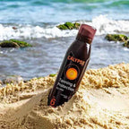 Refect Beauty Calypso Sun Tanning and Protection dry mist SPF6 bottle standing in beach sand with ocean waves behind
