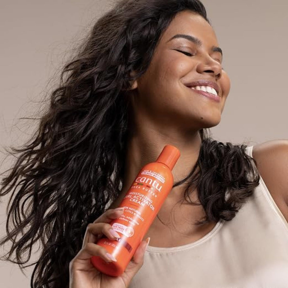 Refect Beauty model smiling with long wavy hair holding an orange bottle of Cantu shea butter curl activator cream