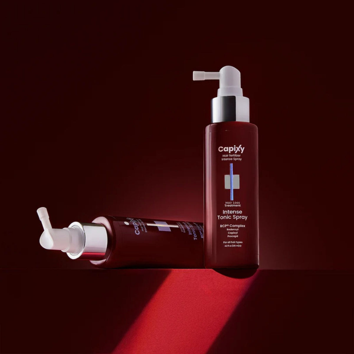 Refect Beauty Capixy Intense Tonic Spray hair loss treatment bottles on a dark red background