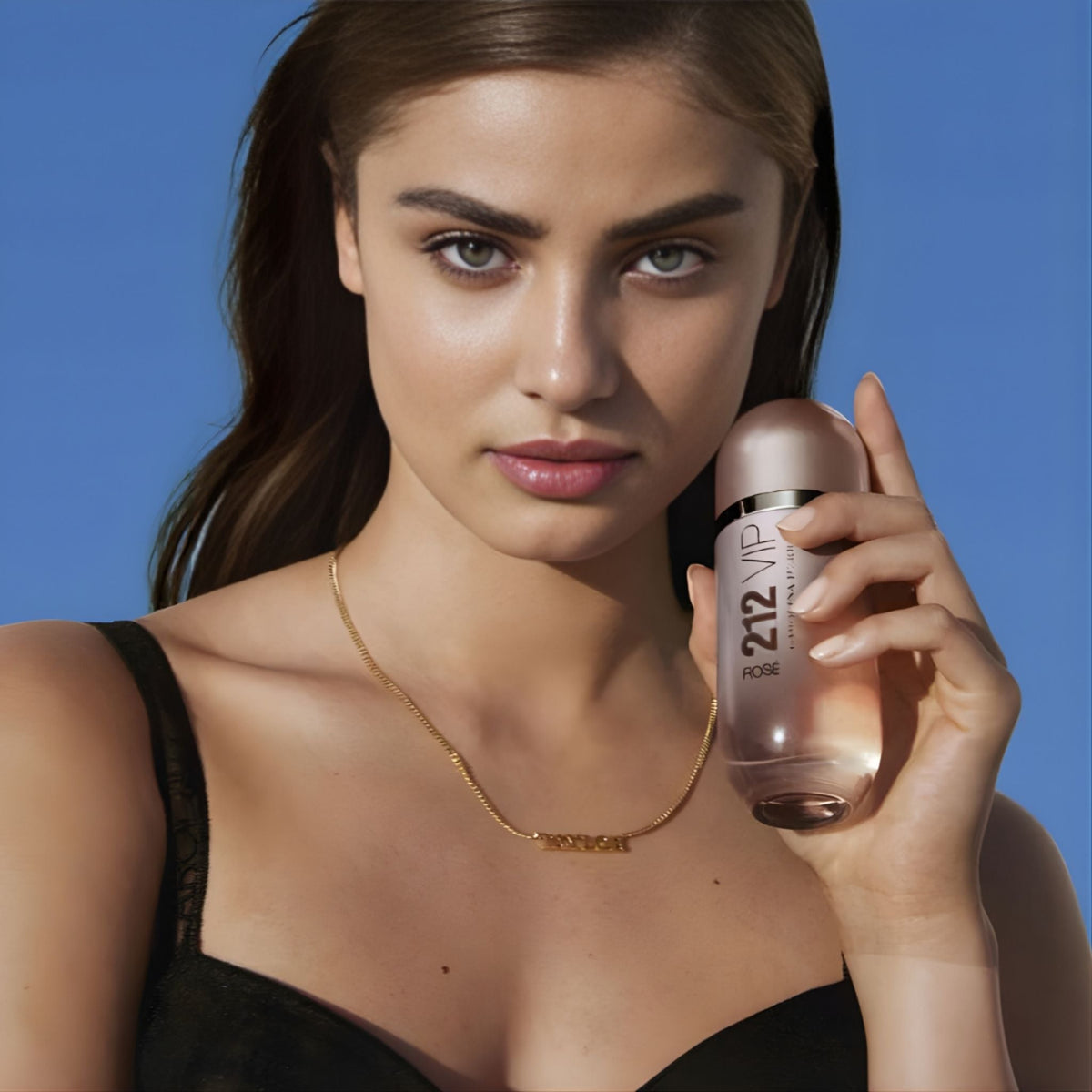 Refect Beauty model holding a bottle of Carolina Herrera 212 VIP Rose Eau de Parfum against a clear blue sky