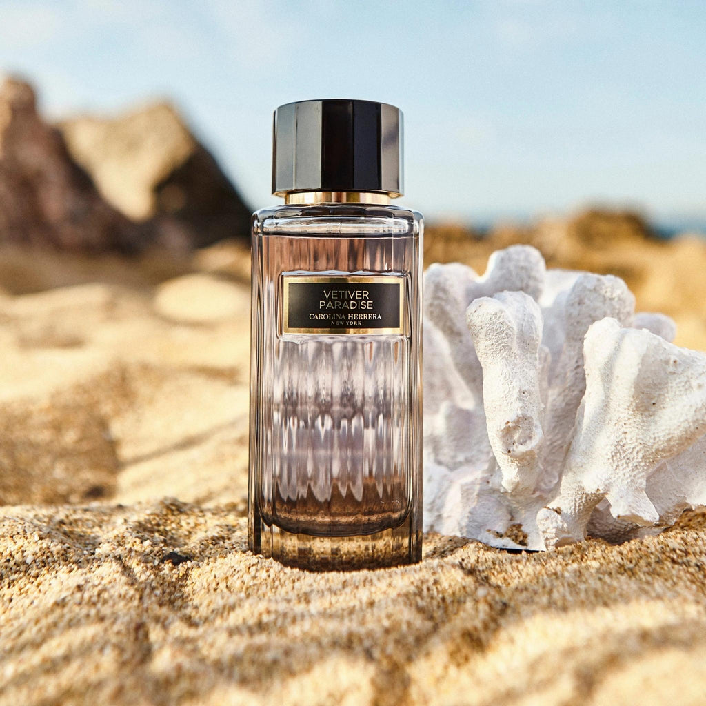 Refect Beauty Carolina Herrera Vetiver Paradise perfume bottle on a sandy beach next to white coral