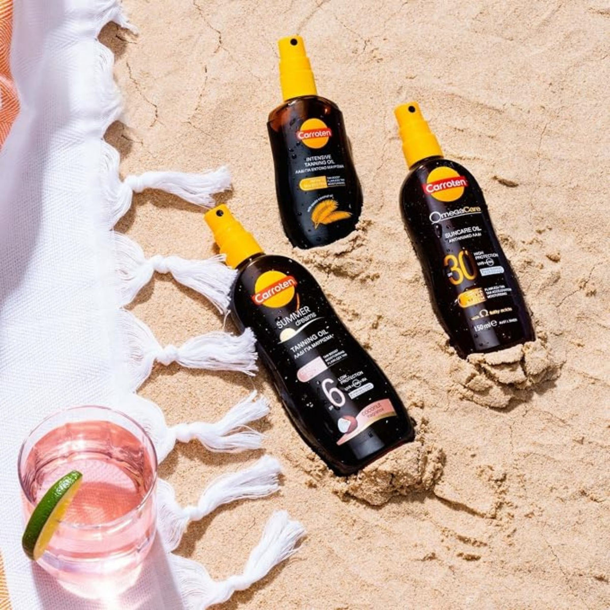 Refect Beauty Carroten tanning oil spray bottles on sandy beach with a glass of lime water and white towel