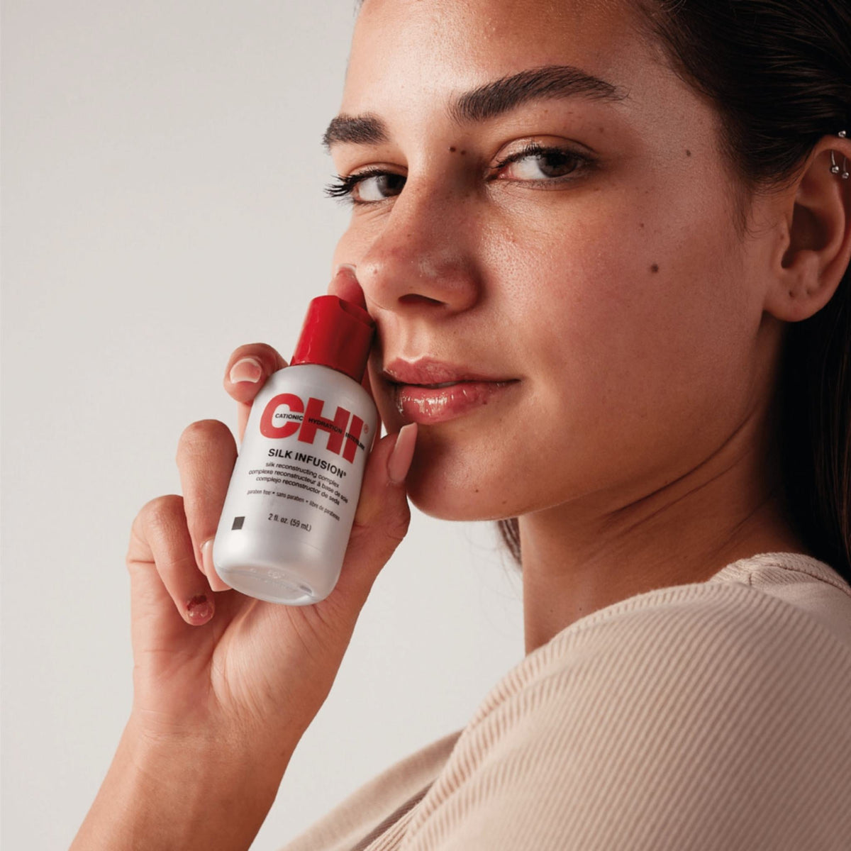 Refect Beauty model holding a bottle of CHI Silk Infusion hair serum against her cheek for a beauty product shot.