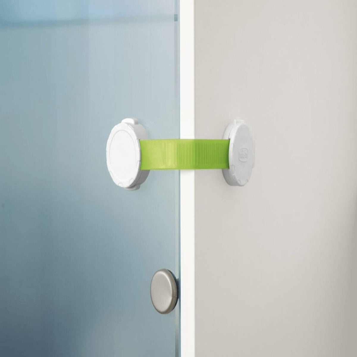 Refect Beauty Chicco child safety cupboard lock with white plastic mounts and an adjustable green strap on a cabinet