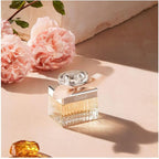 Refect Beauty Chloé Eau de Parfum bottle with a beige ribbon, surrounded by pink peonies on a warm-toned surface.