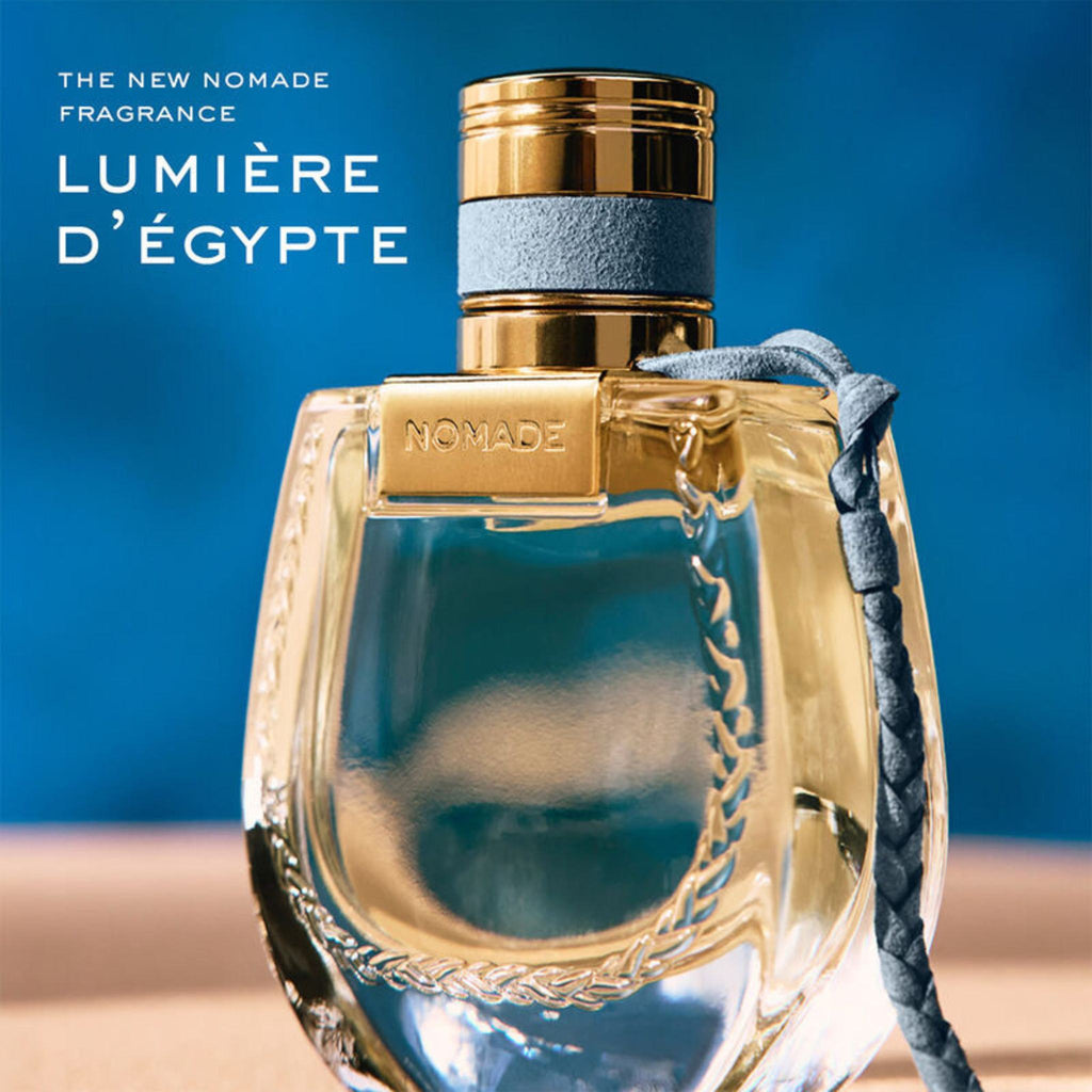 Refect Beauty Chloe Nomade Lumiere D'Egypte perfume bottle with gold cap and grey braided cord on blue background