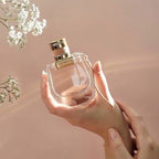 Refect Beauty Chloé Nomade Eau de Parfum glass bottle held in a hand against a soft pink background with baby's breath