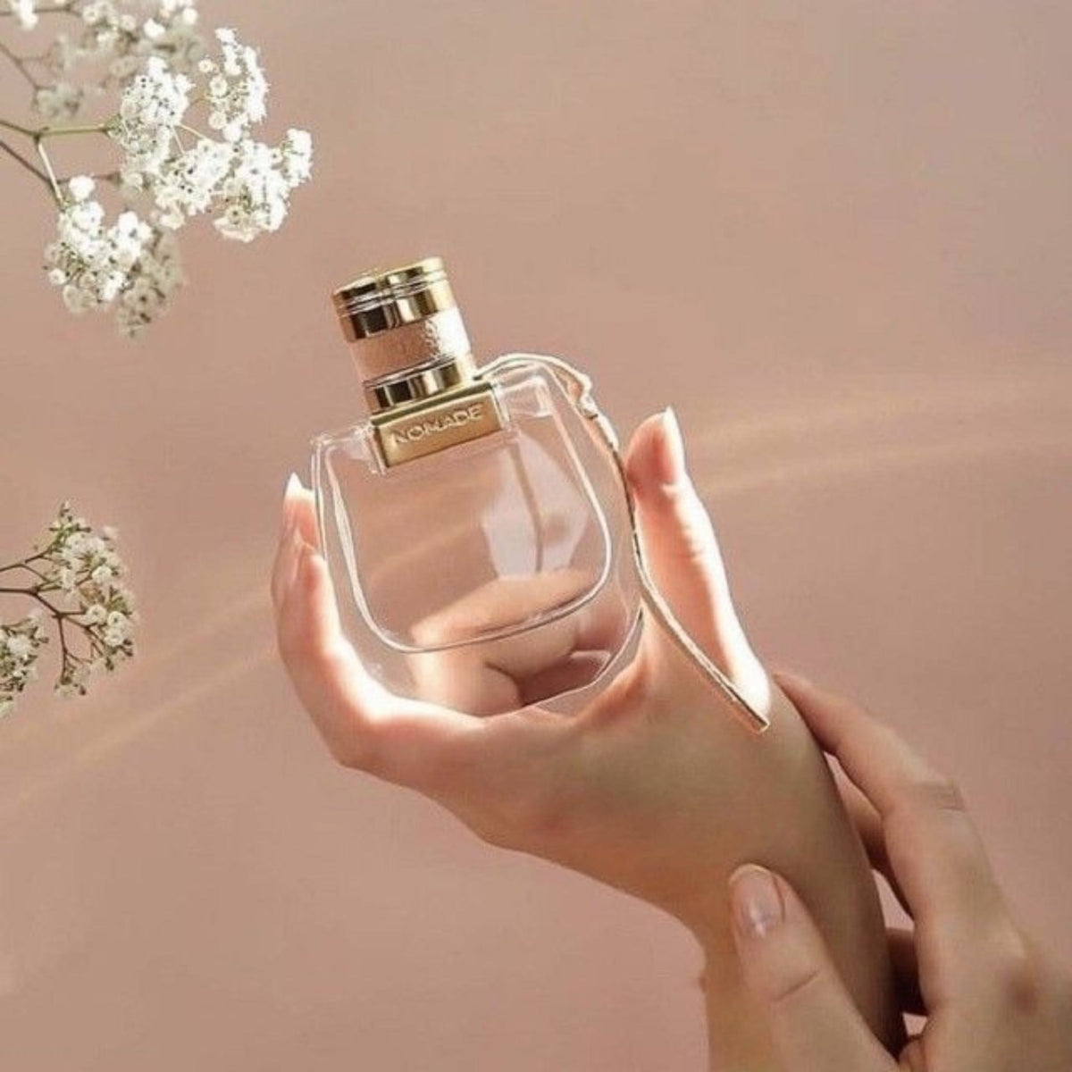 Refect Beauty Chloé Nomade Eau de Parfum bottle held in a hand against a soft pink background with baby's breath