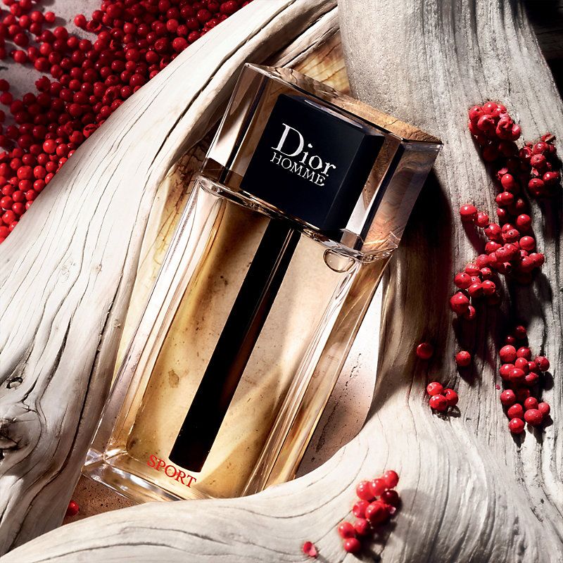 Refect Beauty Dior Homme Sport Eau de Toilette bottle resting on driftwood surrounded by red peppercorns