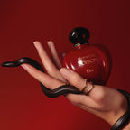 Refect Beauty Dior Hypnotic Poison perfume bottle held in a hand with a black snake against a deep red background.