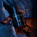 Refect Beauty Dior Sauvage Elixir perfume bottle resting on dark textured rock with a branded Dior ribbon