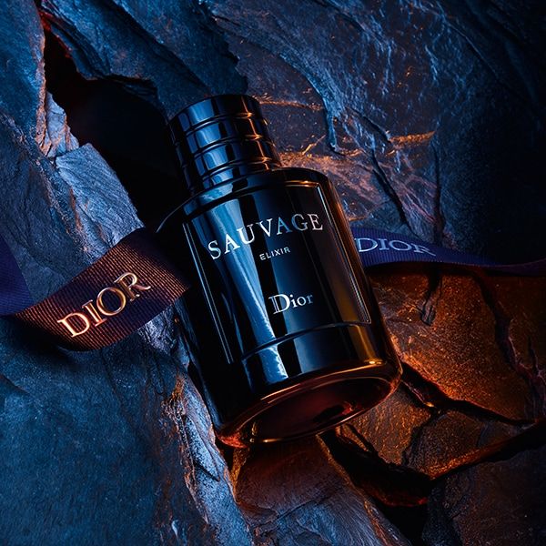 Refect Beauty Dior Sauvage Elixir perfume bottle resting on dark textured rock with a branded Dior ribbon