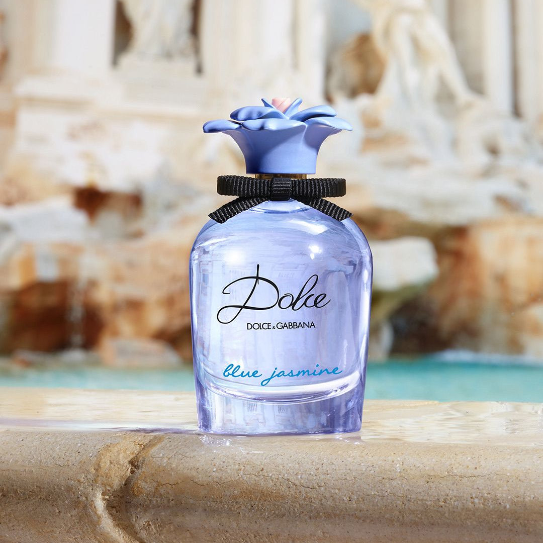 Refect Beauty Dolce & Gabbana Dolce Blue Jasmine perfume bottle with a blue floral cap and black ribbon on a fountain.