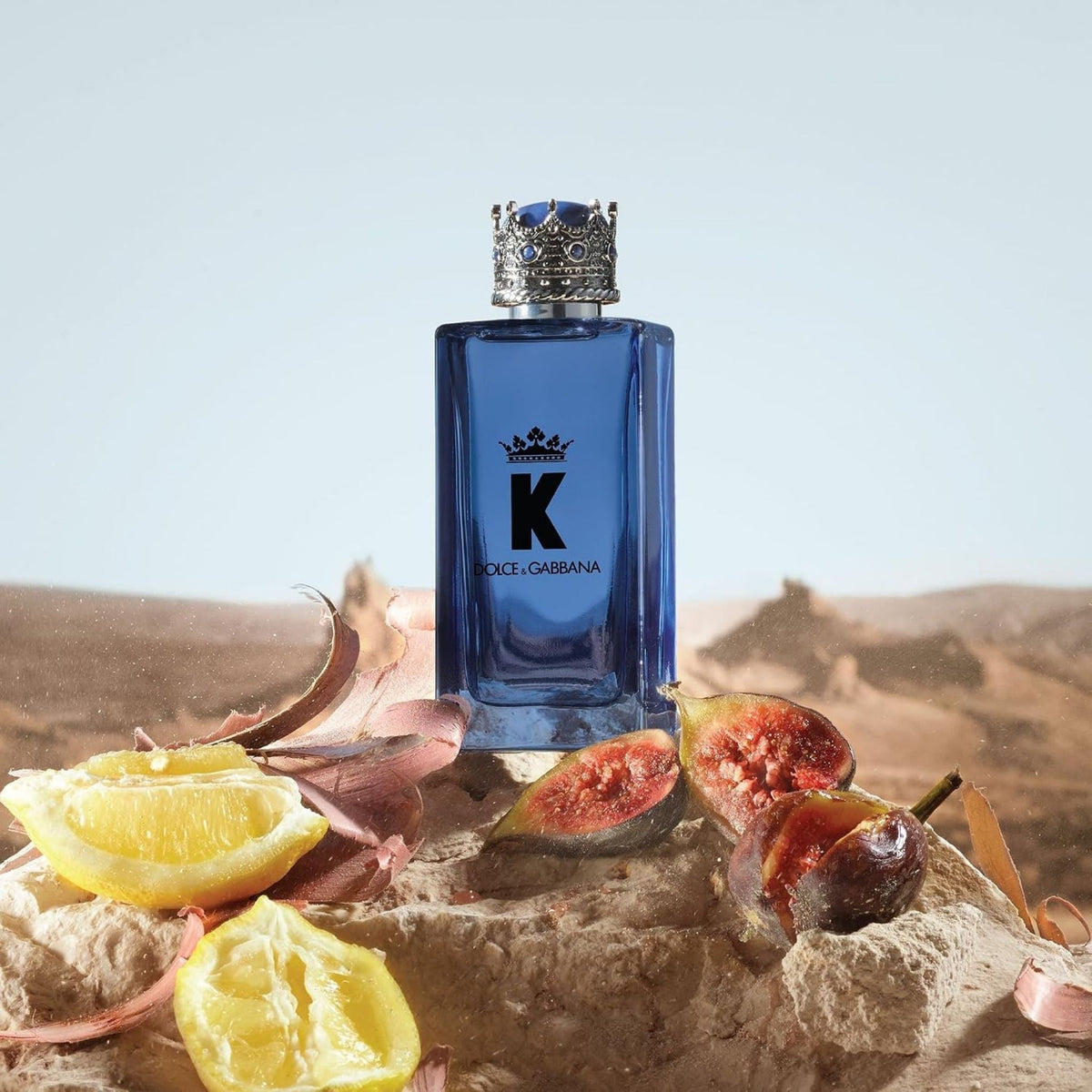 Refect Beauty Dolce & Gabbana K Eau de Parfum bottle with crown cap, displayed on a rock with lemon and fig slices.