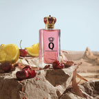 Refect Beauty Dolce & Gabbana Q Eau de Parfum bottle with a crown cap, surrounded by fresh cherries and lemon slices.