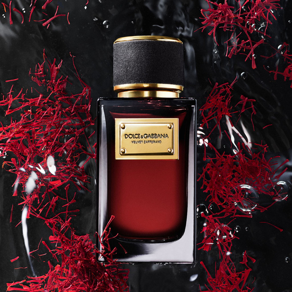 Refect Beauty Dolce & Gabbana Velvet Zafferano perfume bottle surrounded by red saffron threads on a dark wet surface.
