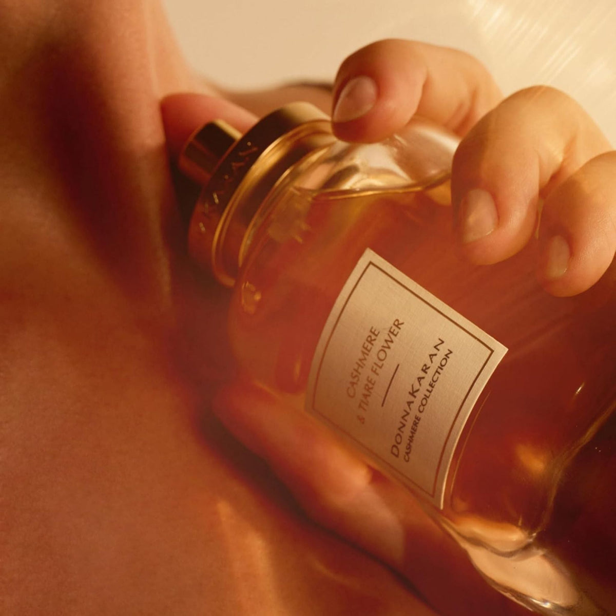 Refect Beauty Donna Karan Cashmere & Tiare Flower perfume bottle held against skin in warm golden lighting