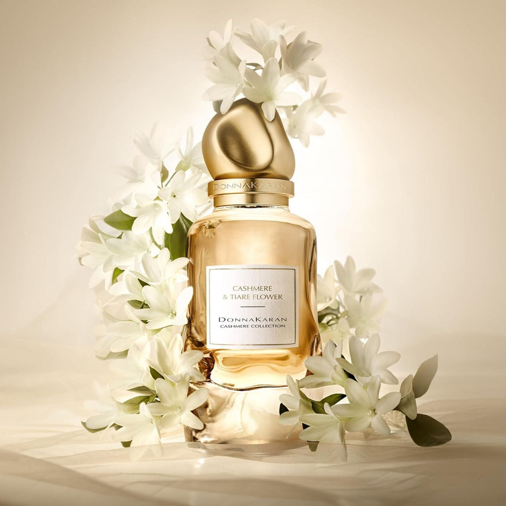 Refect Beauty Donna Karan Cashmere & Tiare Flower perfume bottle surrounded by white tropical flowers on soft fabric