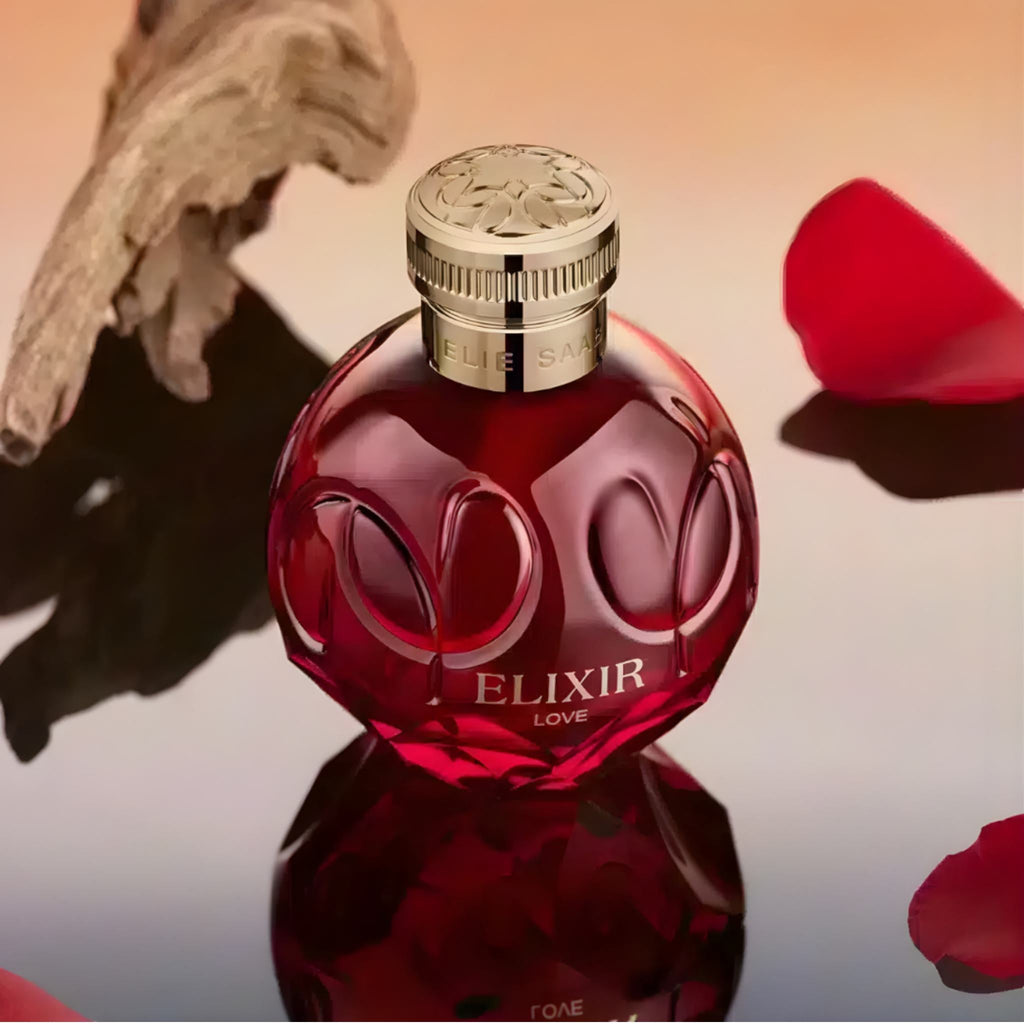 Refect Beauty Elie Saab Elixir Love perfume bottle in deep red glass with gold cap, surrounded by rose petals.