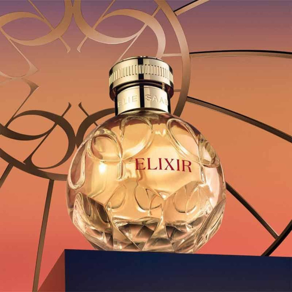 Refect Beauty Elie Saab Elixir Eau de Parfum in a round glass bottle with gold cap against a sunset gradient backdrop