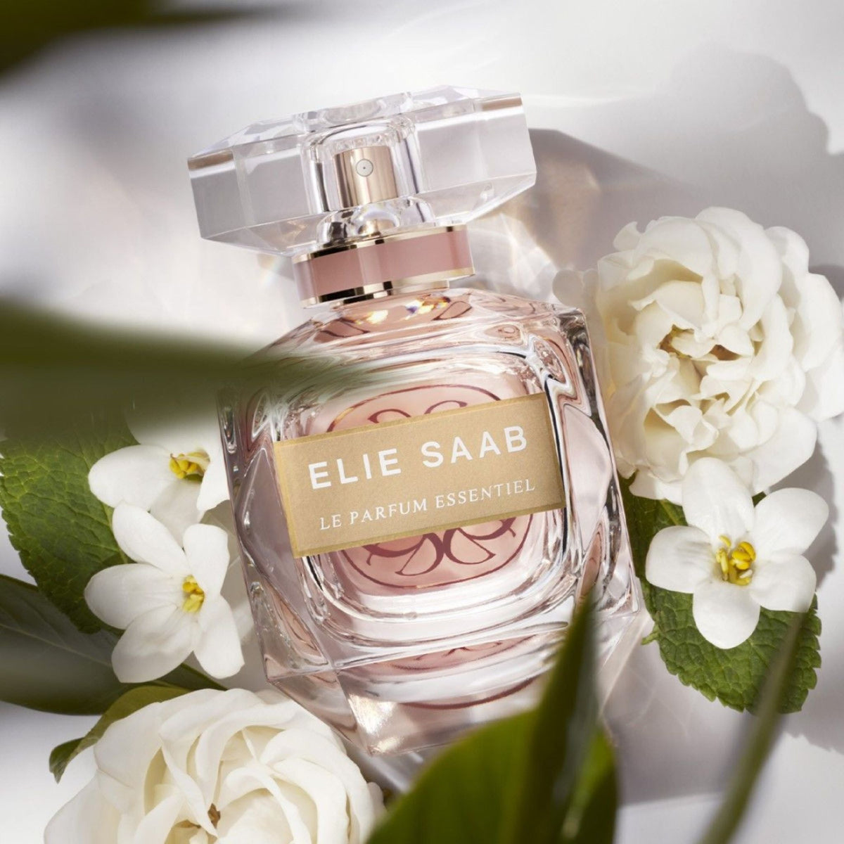 Refect Beauty Elie Saab Le Parfum Essentiel perfume bottle surrounded by white gardenia flowers and green leaves
