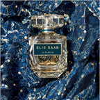 Refect Beauty Elie Saab Le Parfum Royal glass perfume bottle set against a sparkling blue sequined fabric background.