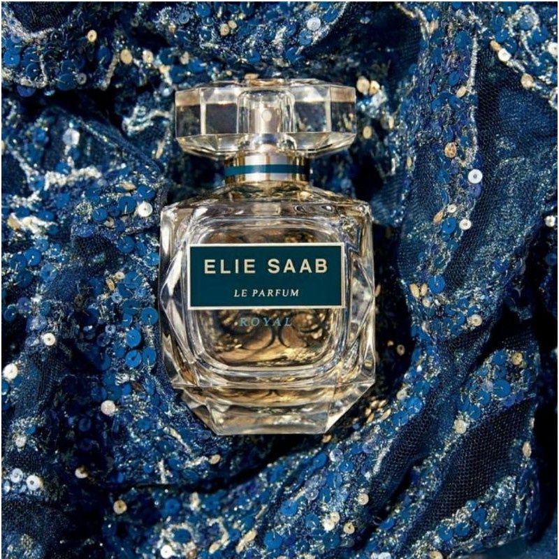 Refect Beauty Elie Saab Le Parfum Royal glass perfume bottle set against a sparkling blue sequined fabric background.