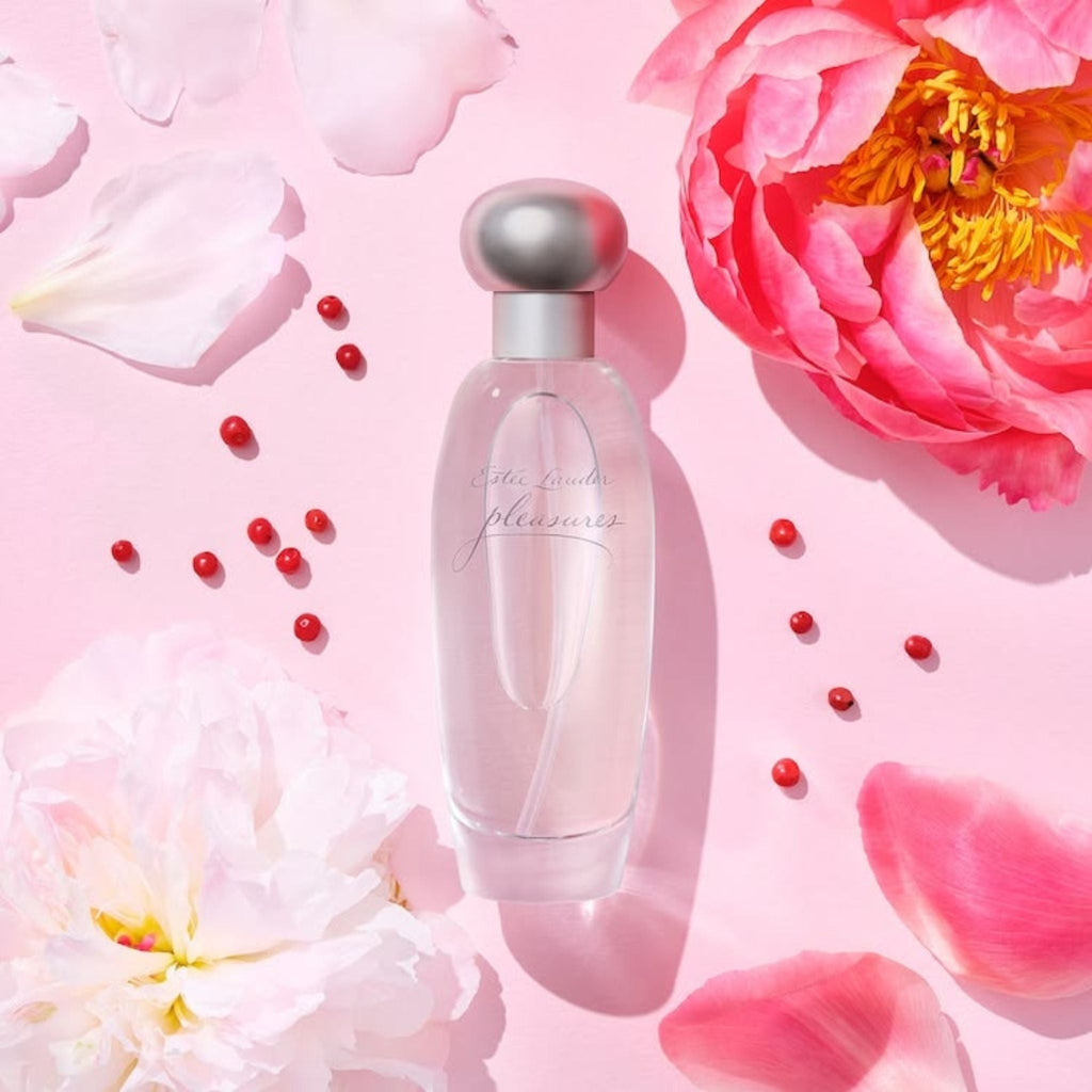 Refect Beauty Estée Lauder Pleasures Eau de Parfum bottle surrounded by pink peony petals and small red berries.