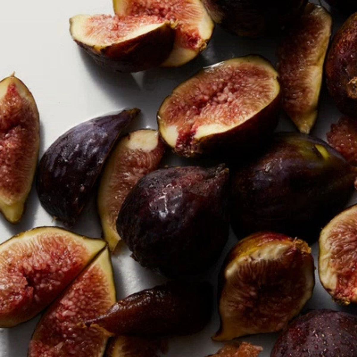 Refect Beauty fresh ripe figs sliced and whole with dark purple skin and pink seeded pulp on a white surface
