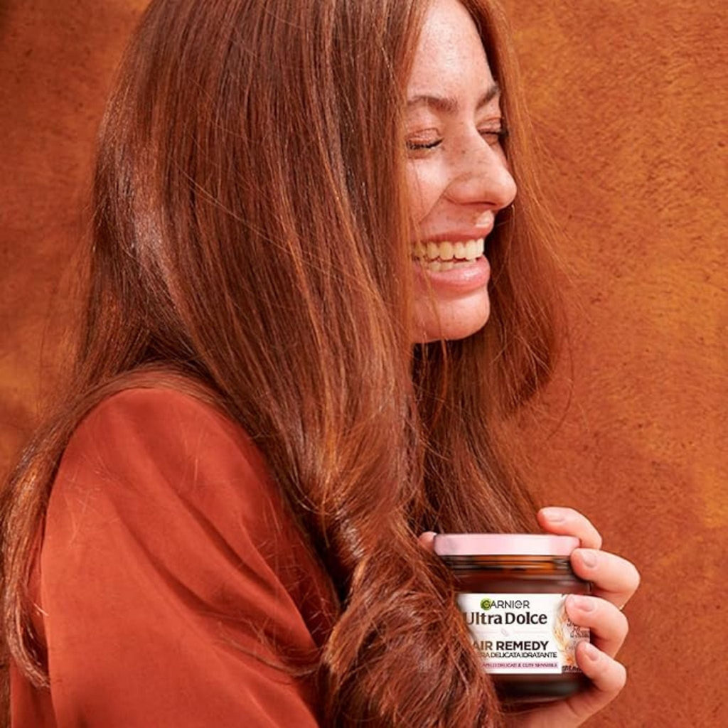 Refect Beauty Garnier Ultra Dolce moisturizing hair mask jar held by a smiling woman with long, healthy red hair.