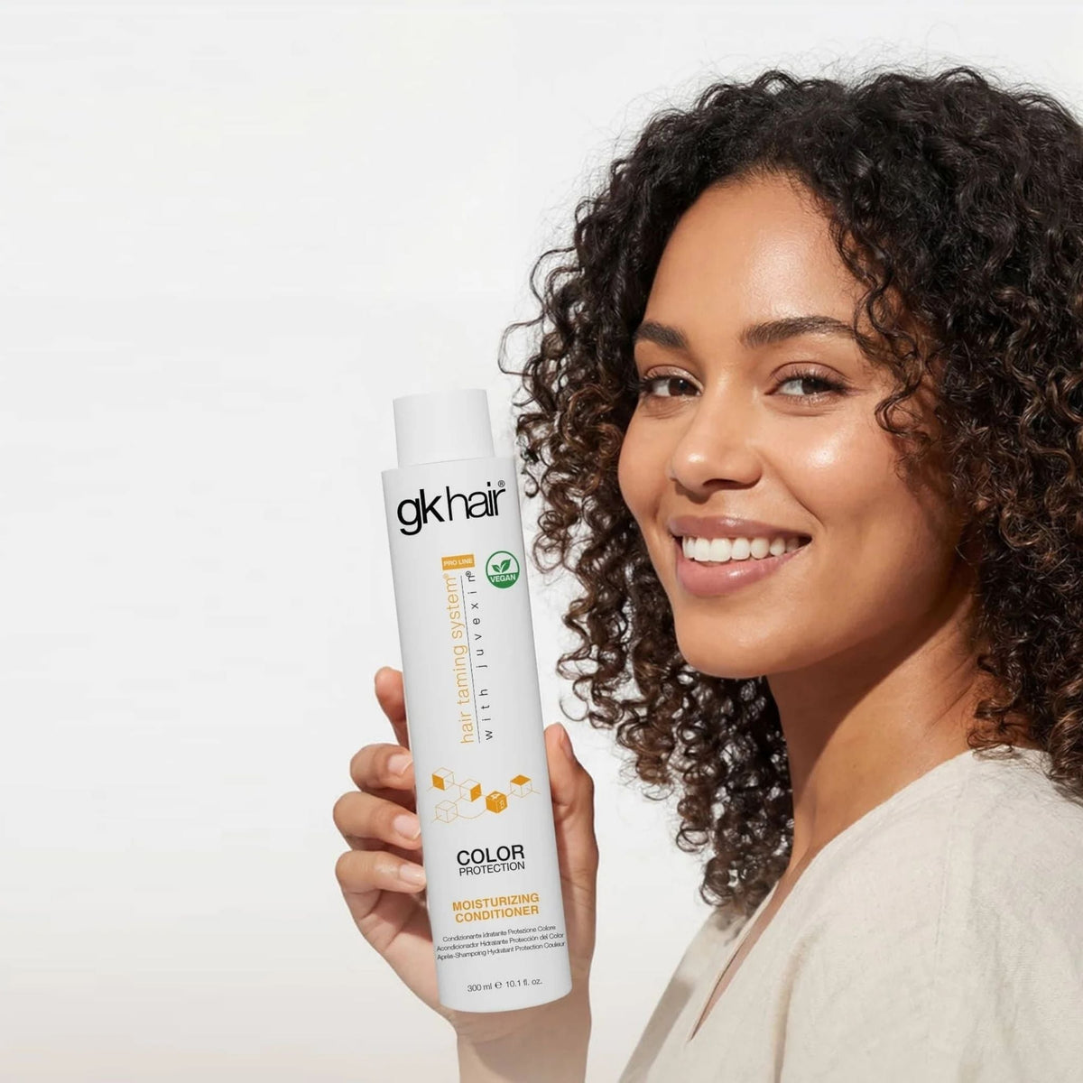 Refect Beauty GK Hair Color Protection Moisturizing Conditioner held by a smiling woman with curly hair