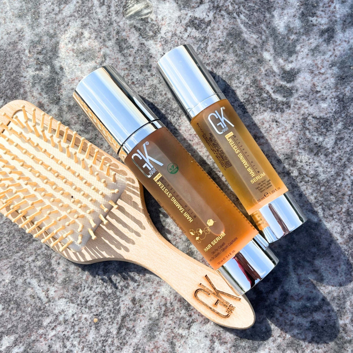 Refect Beauty GK Hair Argan Oil Serum bottles and a wooden hair brush on a stone surface