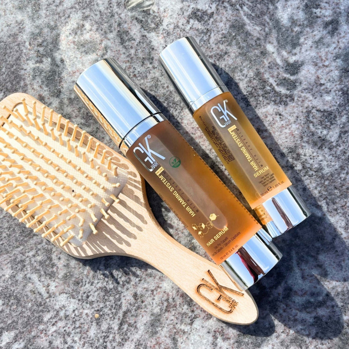 Refect Beauty GK Hair Argan Oil Serum bottles with a wooden hair brush on a stone surface