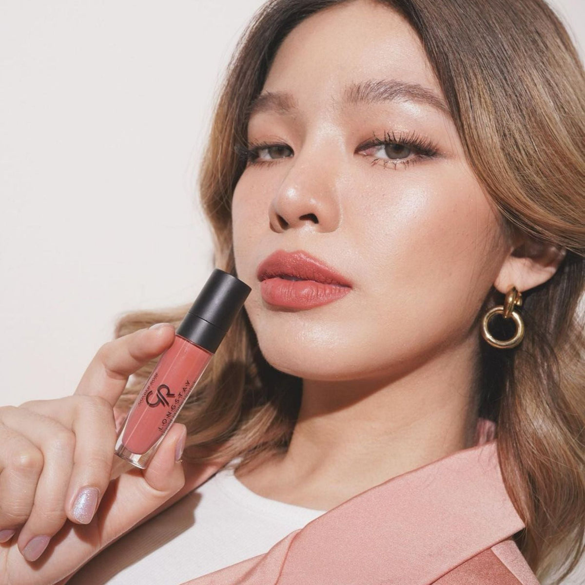 Refect Beauty model holding a Golden Rose Longstay liquid matte lipstick in a soft dusty rose shade