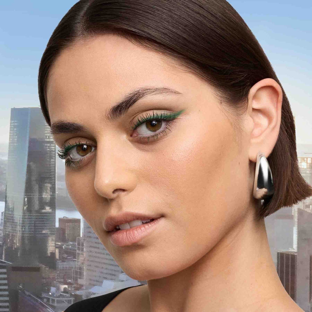 Refect Beauty model wearing Maybelline Sky High green mascara for long, defined lashes against a city skyline backdrop
