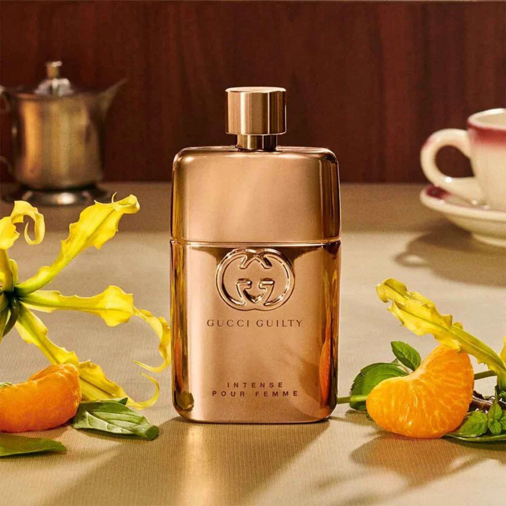 Refect Beauty Gucci Guilty Pour Femme Intense perfume bottle in metallic gold, surrounded by mandarin and flowers.