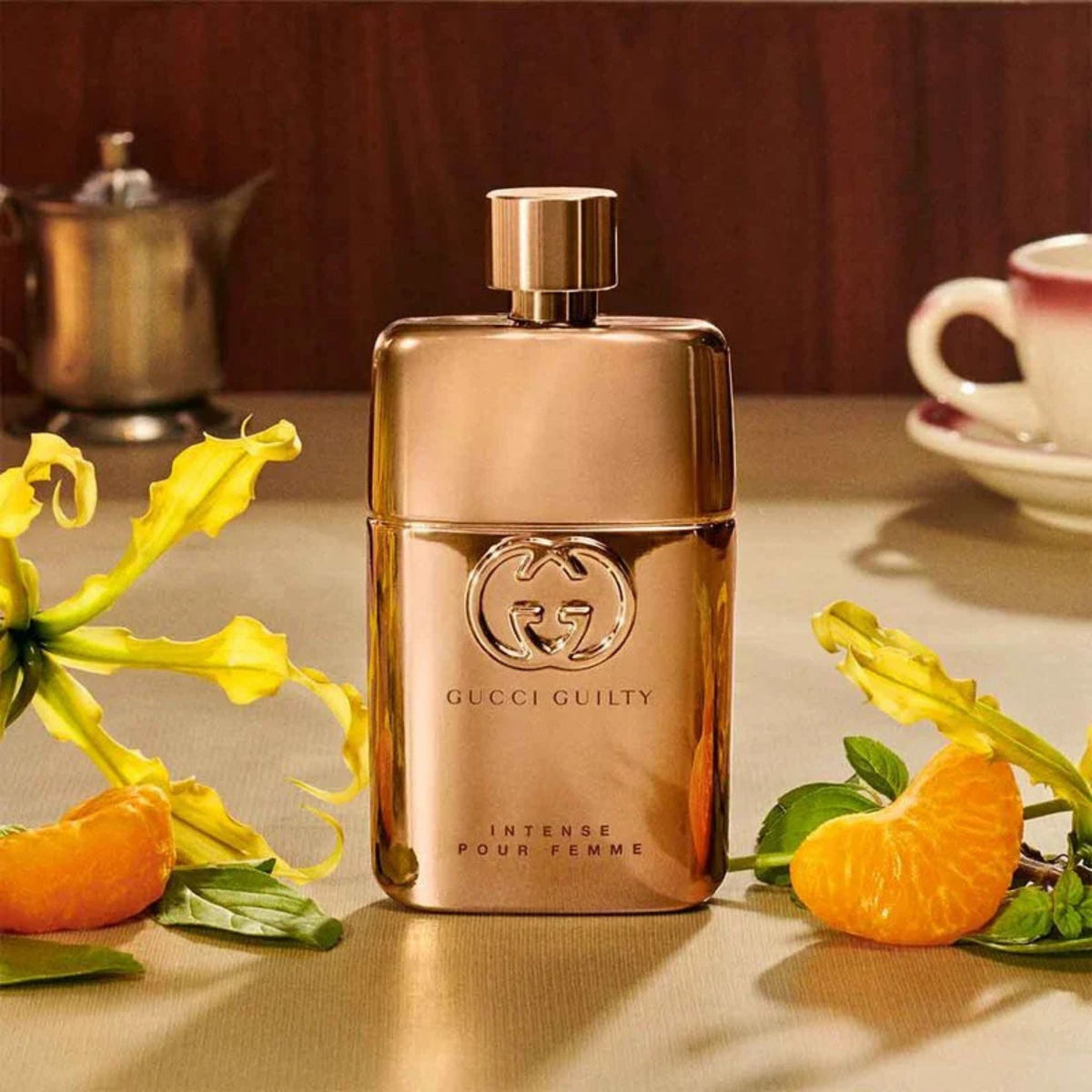 Refect Beauty Gucci Guilty Pour Femme Intense perfume bottle in metallic gold, surrounded by mandarin and flowers.